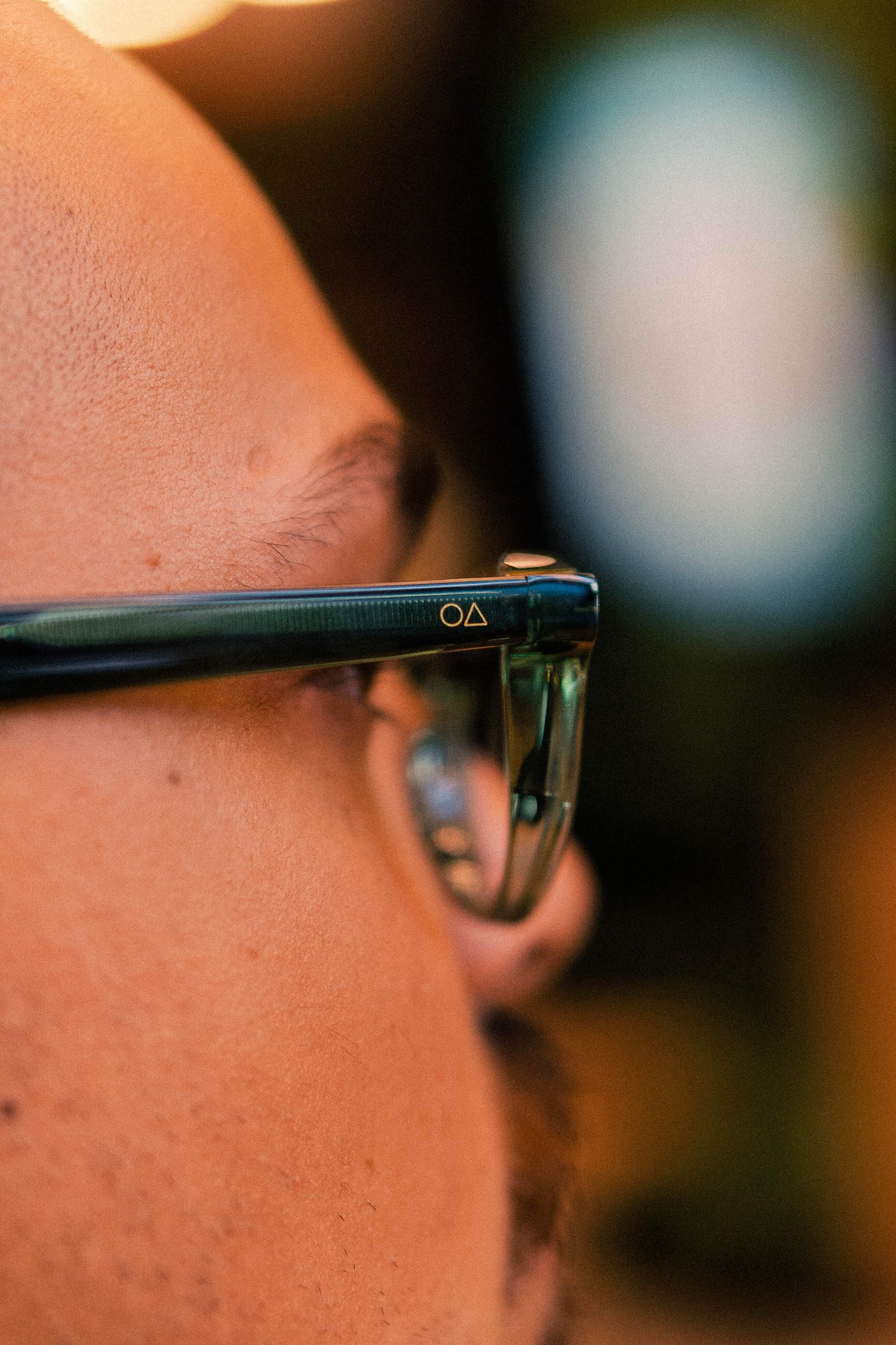 Close de homem usando óculos de grau, focando na haste e na lateral do rosto em ambiente interno.