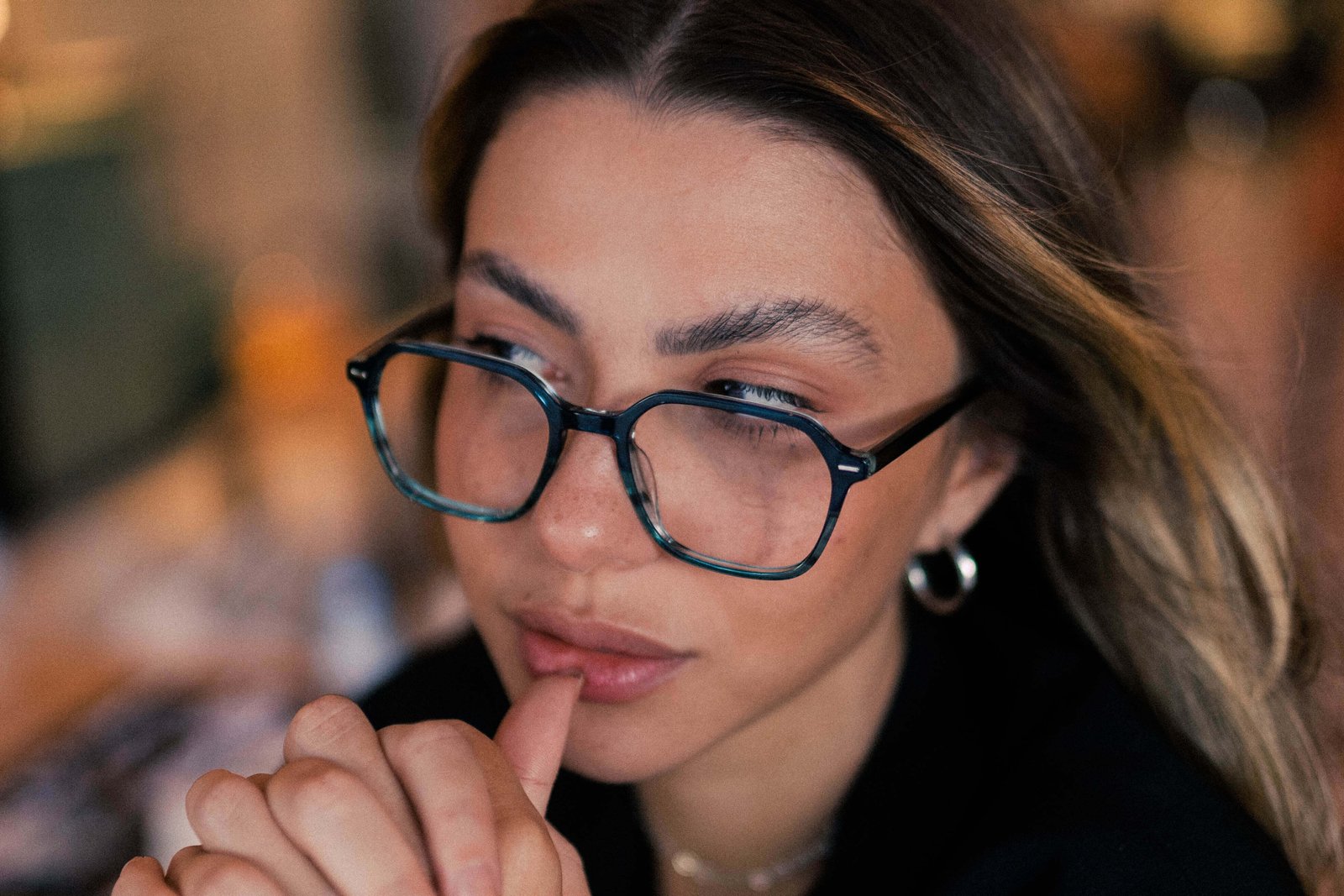 Duas mulheres usando óculos de grau conversando em uma mesa ao ar livre com plantas ao redor.