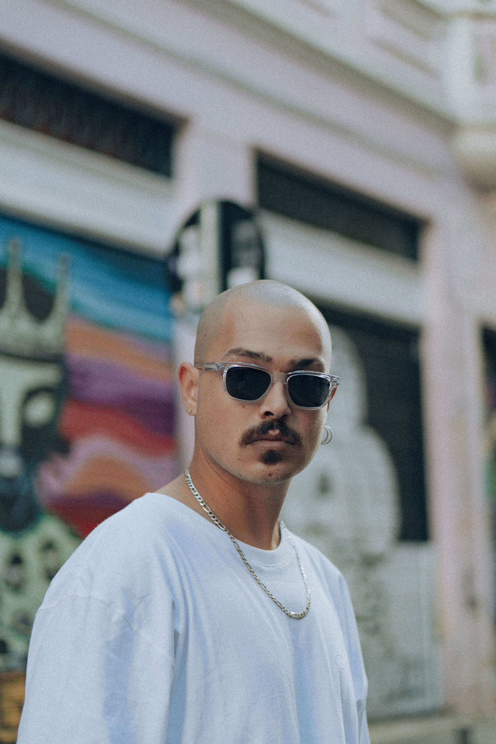 Homem com óculos de sol escuros e corrente prateada olhando sério para a câmera em rua de Curitiba.