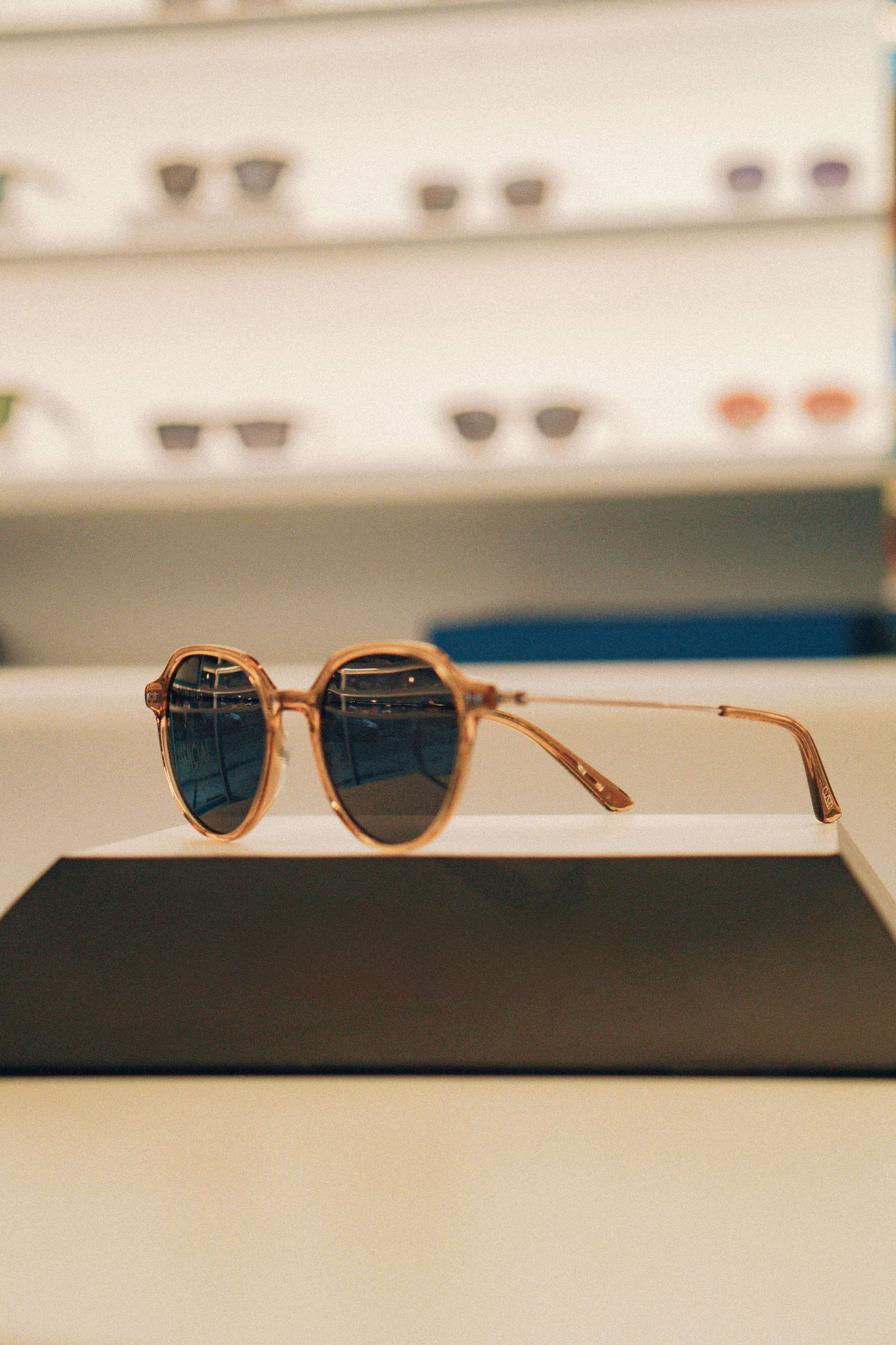 Óculos de sol redondos com armação dourada expostos sobre base preta em vitrine de ótica.