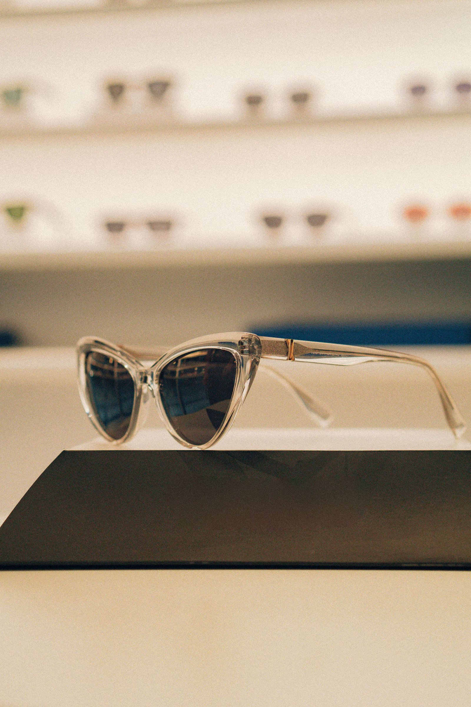 Óculos de sol em formato gatinho metálicos prateados exibidos em prateleira iluminada.