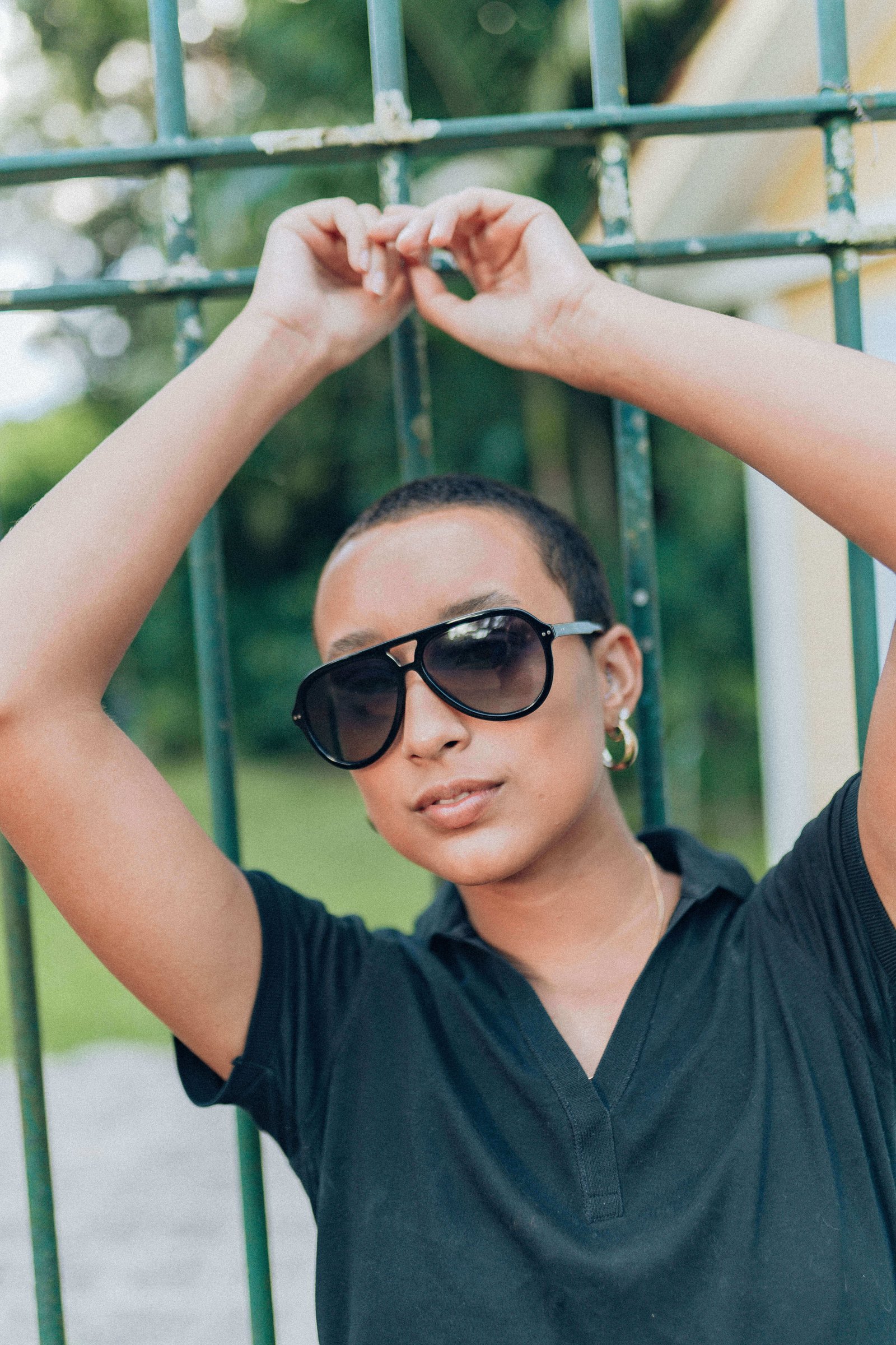 Mesma pessoa de óculos de sol escuros e camiseta preta em pose descontraída segurando a grade.