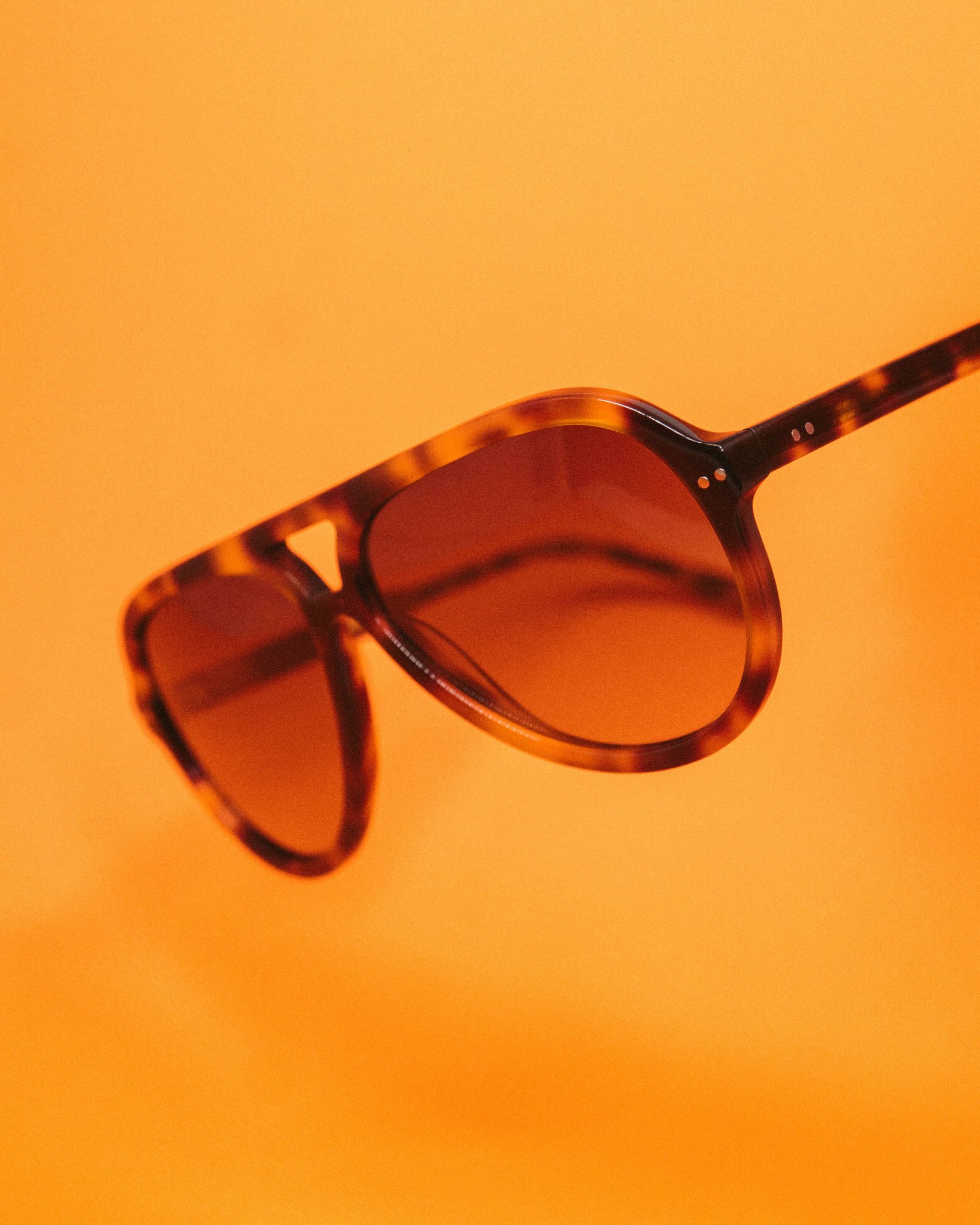 Close de armação de óculos de grau em acetato marrom sobre fundo bege.